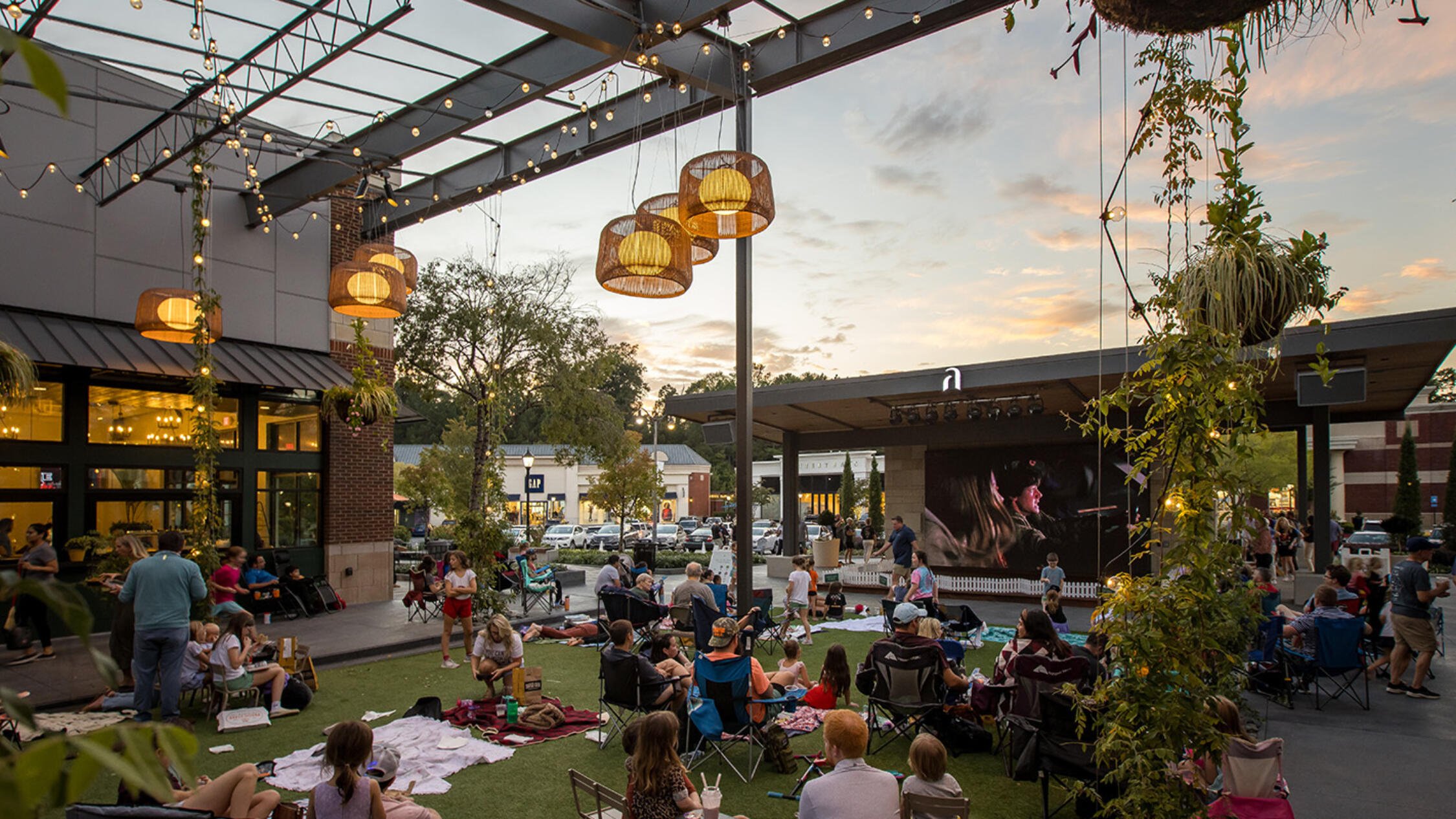 Visitors at Avenue East Cobb sitting on the grass in an outdoor courtyard watching a movie at dusk