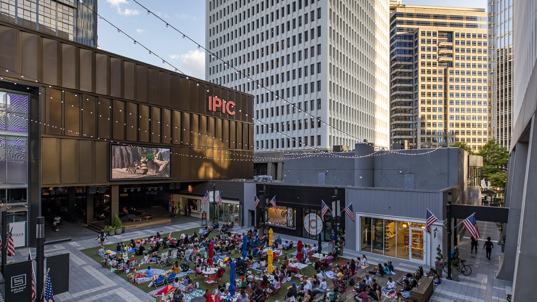 Visitors at Colony Square sitting on the grass in an outdoor courtyard watching a movie at dusk