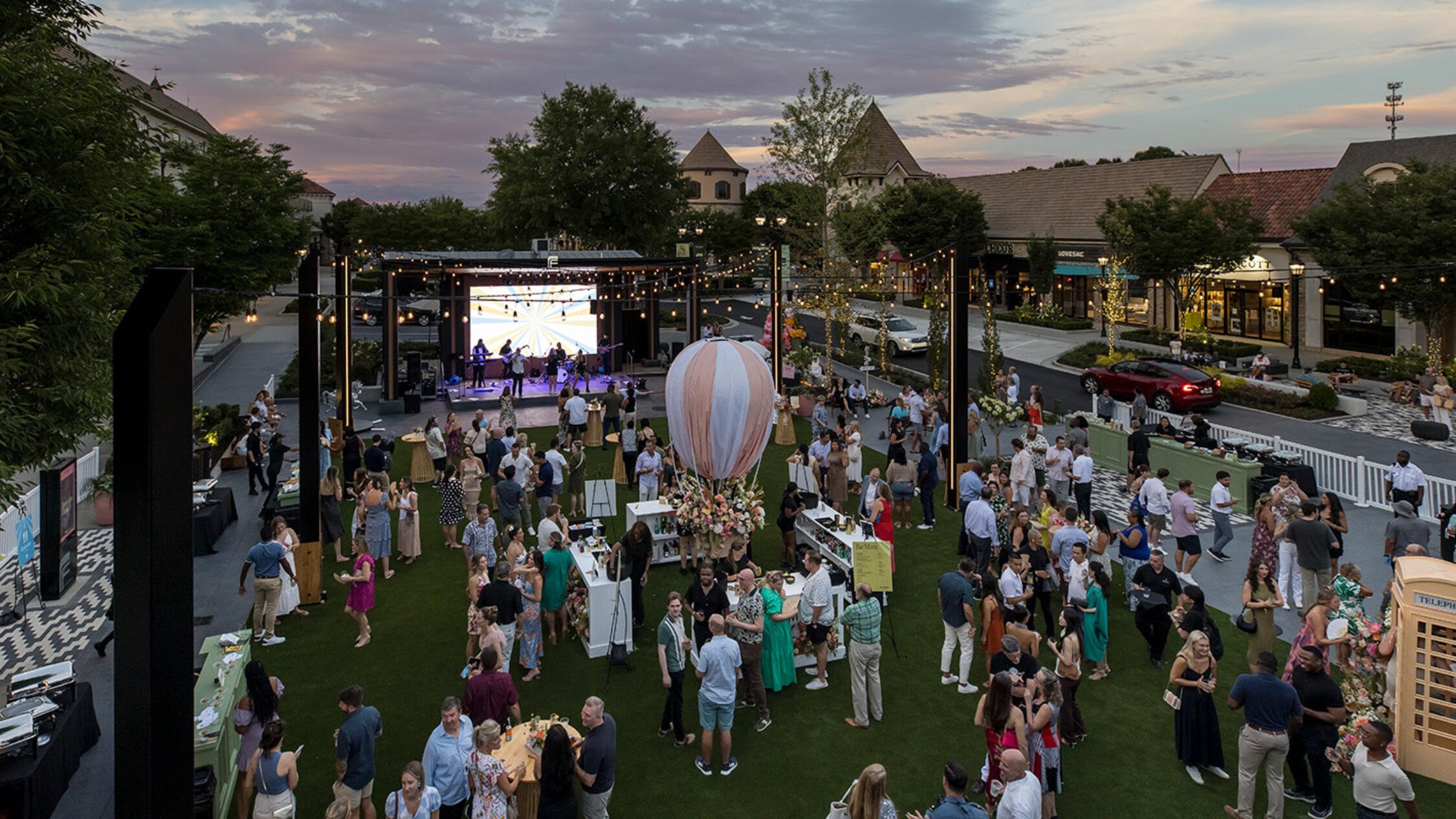 Visitors at The Forum gathered on the grass in an outdoor courtyard watching a live band playing music at dusk