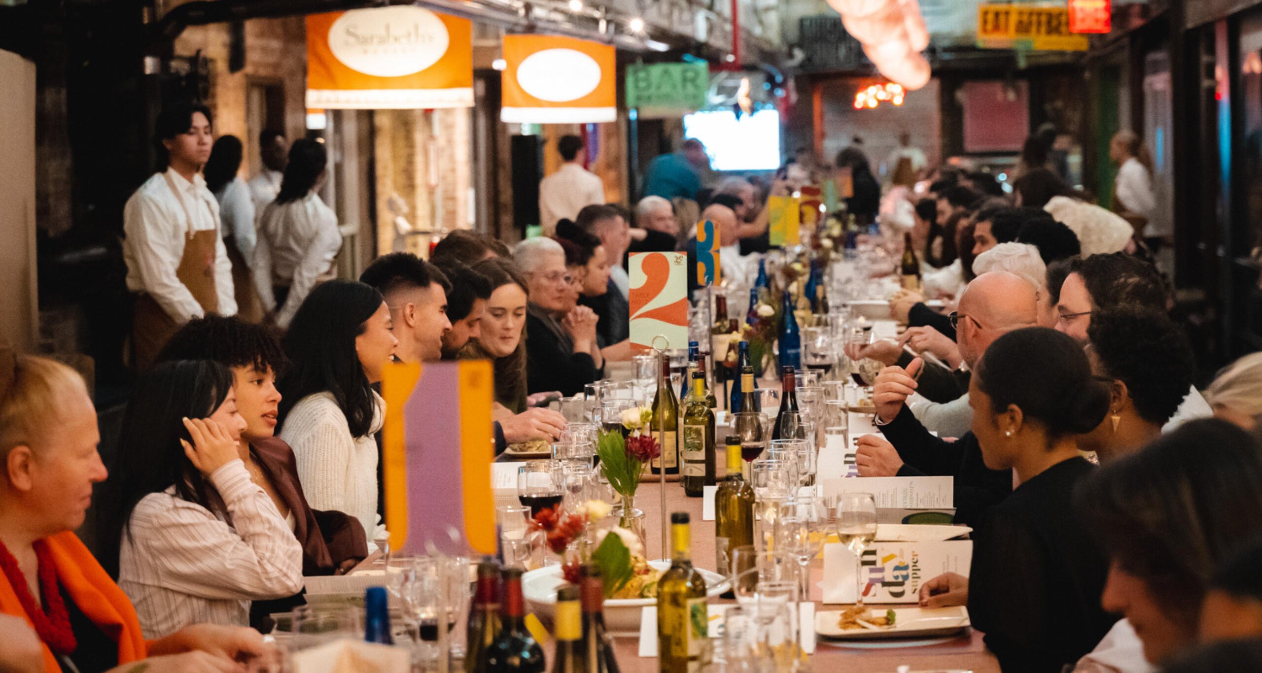 A crowd at a long dining table enjoying Sunday Supper inside Chelsea Market's main concourse