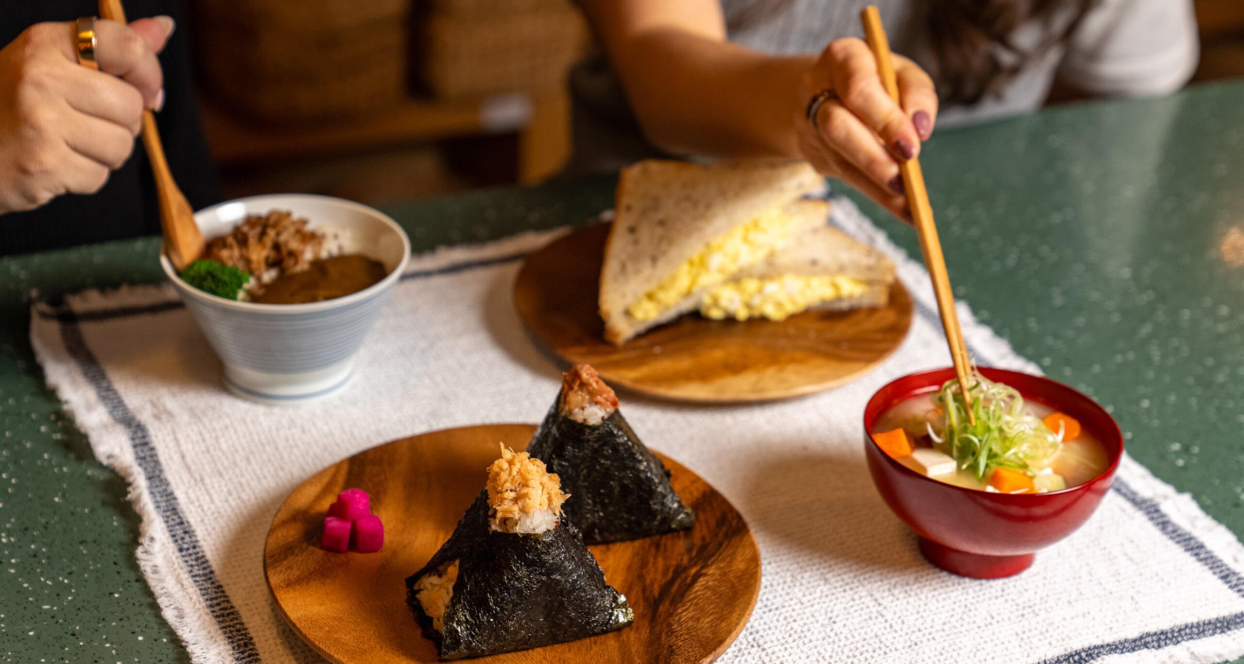 View of hands holding chopsticks reaching for plated food on a table at MUJI in Chelsea Market