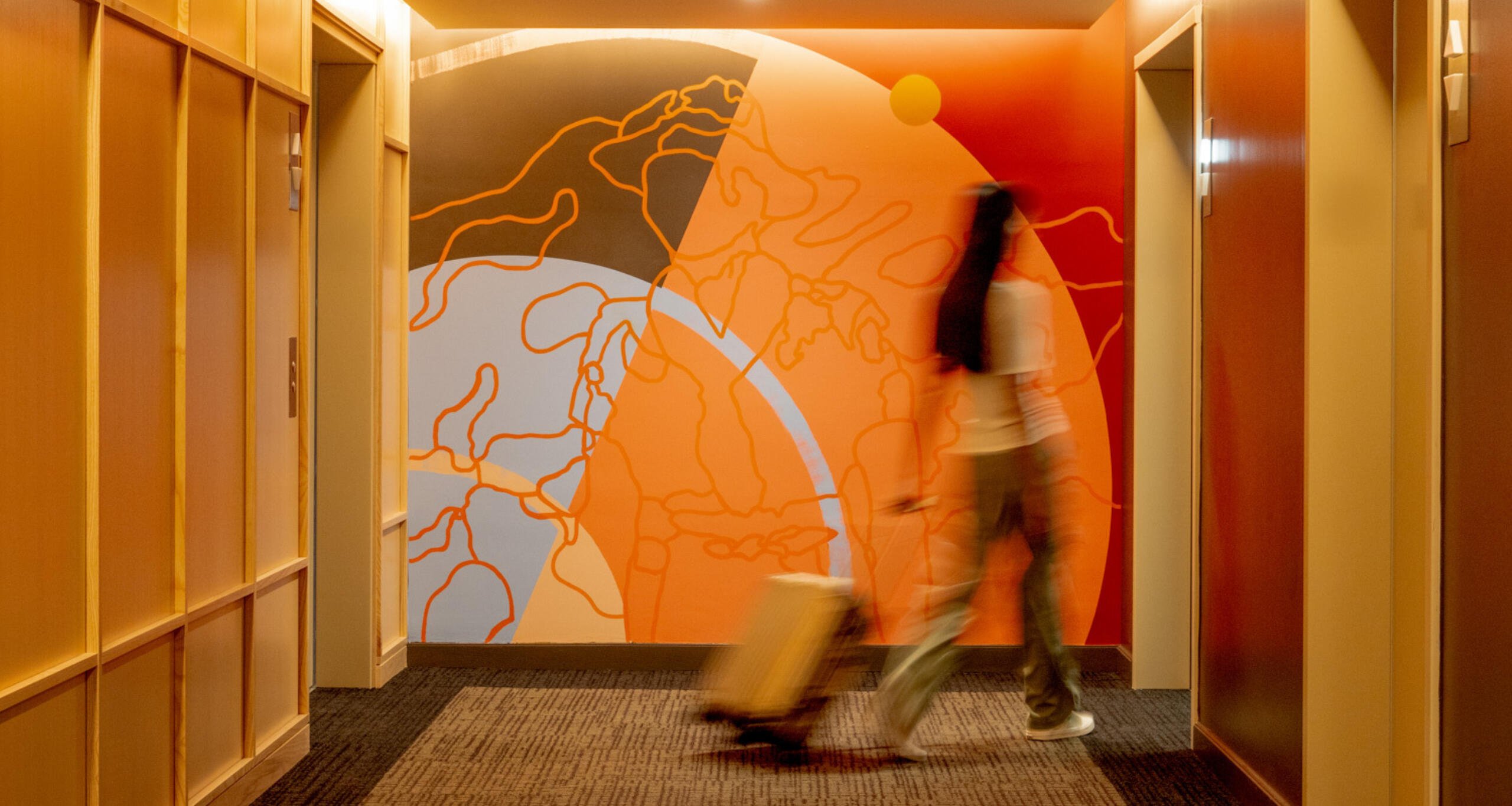 A woman rolling a suitcase from a hallway into a room at Ponce City Market's Scout Living