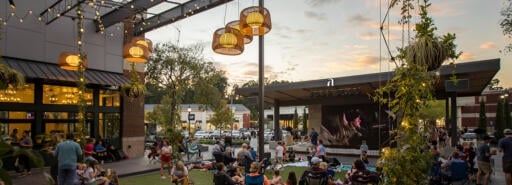 Visitors at Avenue East Cobb sitting on the grass in an outdoor courtyard watching a movie at dusk