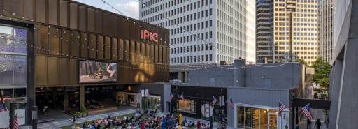 Visitors at Colony Square sitting on the grass in an outdoor courtyard watching a movie at dusk