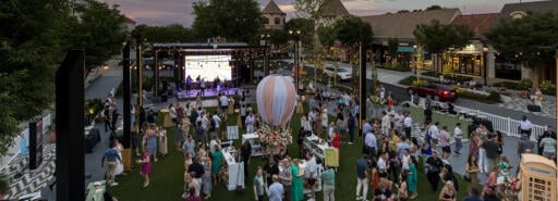 Visitors at The Forum gathered on the grass in an outdoor courtyard watching a live band playing music at dusk