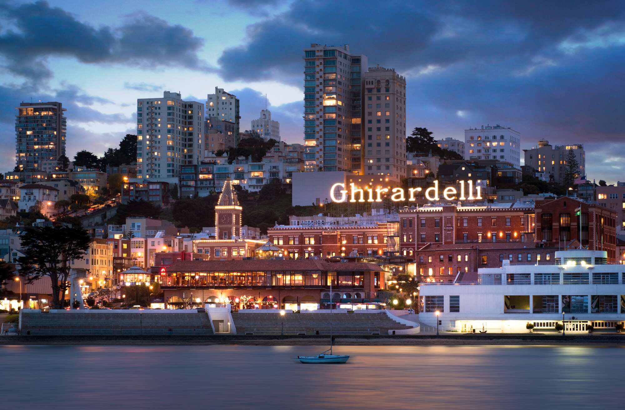 ghirardelli-square-exterior-at-dusk-with-bay-in-foreground-and-skyline